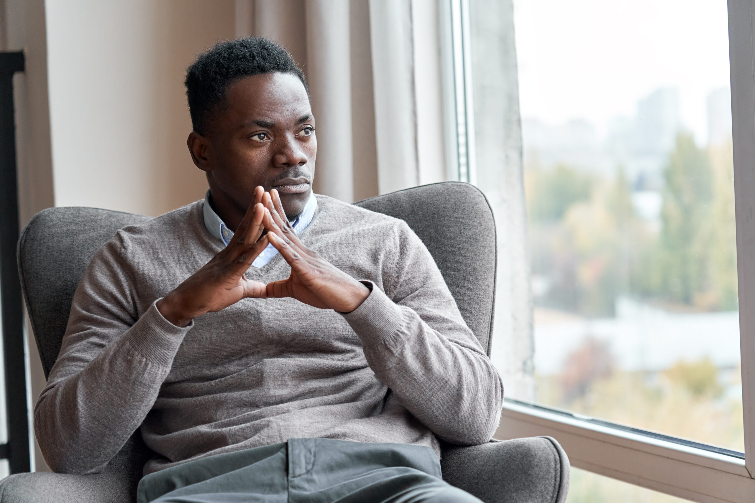 Confident serious focused stylish rich african black man sitting in chair at home looking away through window dreaming thinking of success, leadership, business vision, planning future in luxury life.